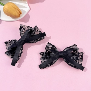 Close-up of black lace bow hair clips with floral embroidery on pink background