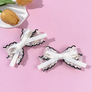Detail of white lace bow hair clips with black pleated edges on a pink background