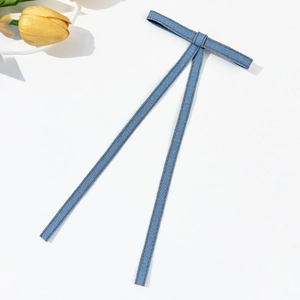 Detailed macro view of denim bow hair clip with brown contrast stitching on white background