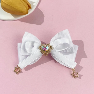 Détail d'une barrette à nœud en satin blanc avec strass en cœur et breloques étoiles