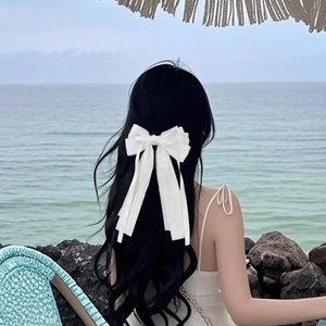 Vue détaillée d'une élégante pince à cheveux à double nœud blanc sur de longs cheveux ondulés