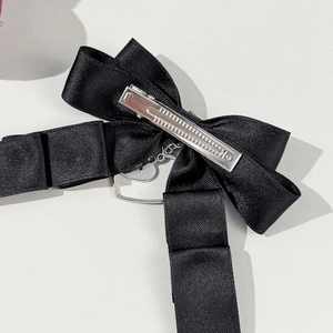Détail de la pince crocodile argentée sur le nœud en satin noir et pendentif cœur