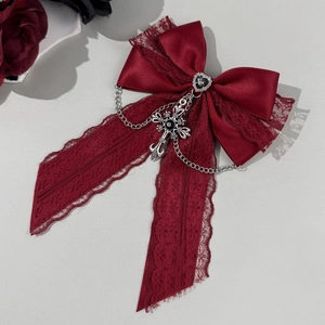 Détail du nœud en dentelle rouge foncé avec pierre cœur, chaîne et croix argentée