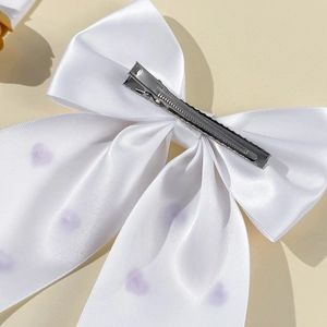 Détail de la pince métallique argentée sur un nœud en satin blanc avec motifs cœurs