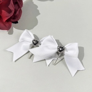 Detailed macro view of white satin bow hair clips with black heart gem and cross charms