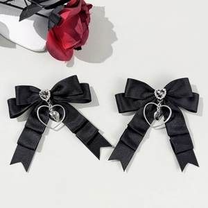Détail de barrettes nœuds en satin noir avec cœur en strass et pendentifs croix argentés