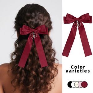 Detail of burgundy satin bow hair clip with heart cross pendant on wavy hair