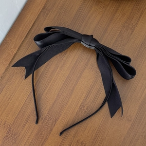 Vue détaillée du serre-tête avec nœud en satin noir superposé sur table en bois