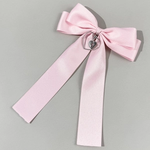 Detail of pink satin bow hair clip with silver heart pendant and engraved cross
