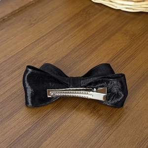 Elegant large black satin bow hair clip with silver metal alligator clip on wood background