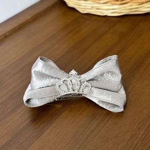 Silver grey silk bow hair clip with sparkling rhinestone crown on a wooden surface
