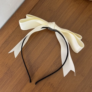 Détail du nœud en satin crème et du serre-tête noir fin sur fond en bois texturé