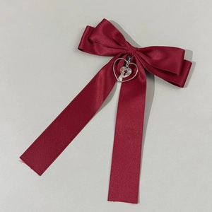 Detail of burgundy satin bow hair clip with silver heart and cross pendant