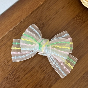 Detailed close-up of rainbow embroidered white mesh bow hairclip on a dark wood surface
