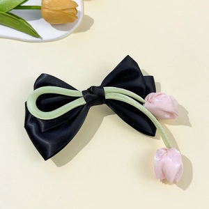 Détail d'une pince à cheveux avec nœud en satin noir et boutons de tulipes roses