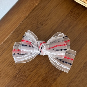 Detail of white mesh bow hair clip with colored polka dot lines on a wooden surface