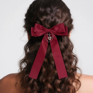 Elegant wine red satin bow hair clip with heart cross pendant on wavy brown hair