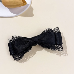 Close-up of black satin bow hair clip with lace edging on elegant aesthetic background