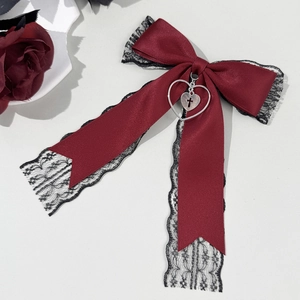 Détail du nœud en satin rouge avec dentelle noire et pendentif cœur croix argenté