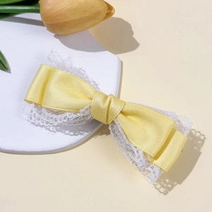 Detailed close-up of yellow ribbon bow hair clip with white lace trim on display stand