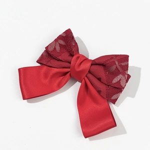 Close-up of red festive bow hair clip with layered satin and floral lace textures