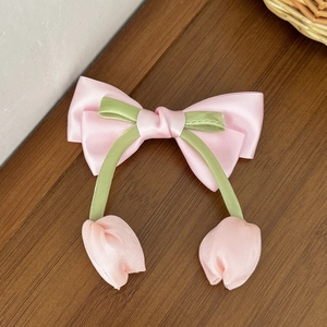 Dettaglio molletta per capelli con fiocco a tulipano rosa in raso su legno antico