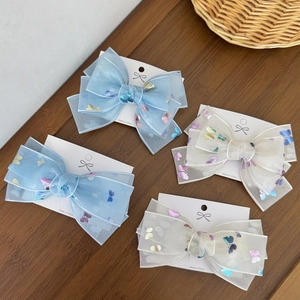 Detail of four mesh bow hair clips in light blue and beige with butterfly patterns