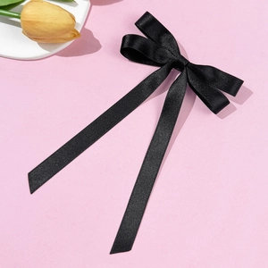 Detail of elegant black satin ribbon bow hair clip with long streamers on pink background