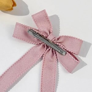 Elegant pink ribbon bow hair clip with lace edges on a minimalist white background