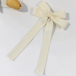 Close-up of cream bow hair clip featuring delicate scalloped edges and textured fabric