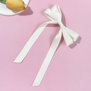 Macro shot of a long white satin ribbon bow hair clip on a pink decorative background