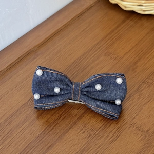 Barrette nœud en jean avec perles blanches et surpiqûres sur surface en bois
