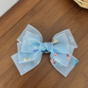 Light blue mesh bow hair clip with colorful metallic butterfly patterns on a wood surface