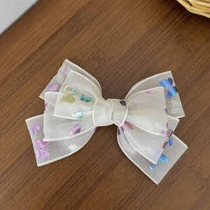 Detail view of a multi-layered white mesh bow hair clip with colorful butterfly patterns