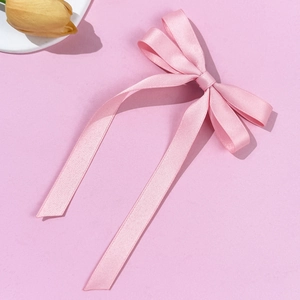 Close-up of pink satin ribbon bow hair clip with long streamers on pink background
