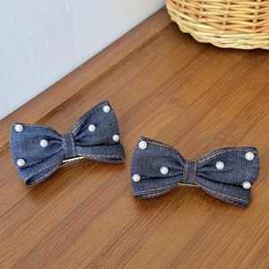 Vue détaillée de deux barrettes nœuds en denim avec perles blanches et coutures orange