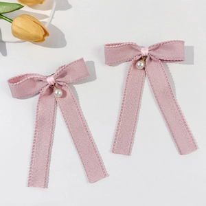 Detailed close-up of light pink bow hair clips with pearls and long tassel ribbons