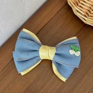 Haarspange aus Denim-Schleife mit Kirschstickerei und gelbem Band auf dunklem Holz