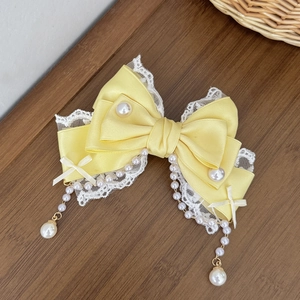 Vue détaillée d'une pince à cheveux avec nœud en satin jaune, dentelle et perles
