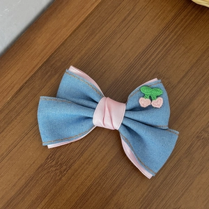 Détail d'une pince à cheveux nœud en denim avec rubans roses et motif de cerises