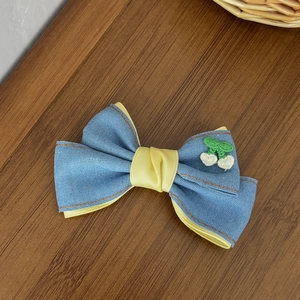 Détail d'une pince à cheveux nœud en denim avec doublure jaune et broderie de fruits