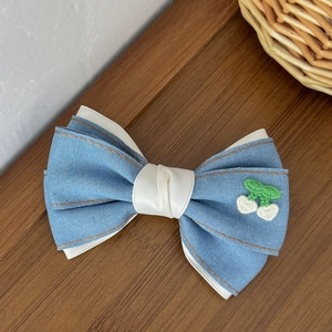 Detailaufnahme der blauen Denim-Haarschleife mit Kirschstickerei und orangen Ziernähten