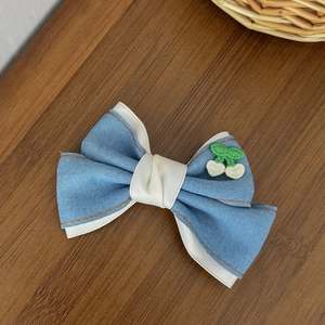 Détail d'une barrette noeud en denim avec coutures orange et broderie cerise sur bois