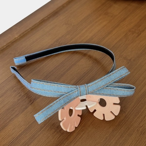 Detail of blue denim headband featuring orange stitching and a pink flower ornament