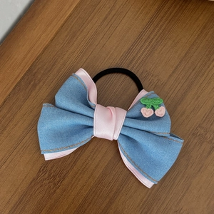 Chouchou en jean avec broderie cerise et ruban rose sur un bureau en bois brun