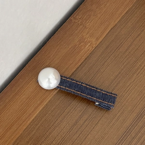 Detail van een blauwe denim haarclip met een grote witte parel en oranje dubbele stiksels