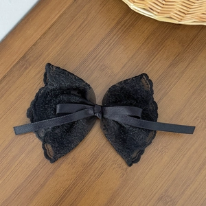 Macro view of a delicate black lace bow hair clip with satin ribbon on a wood surface