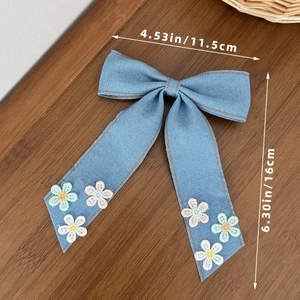 Barrette à cheveux avec nœud en denim bleu et marguerites brodées sur une table en bois