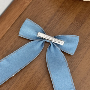 Barrette nœud en jean bleu avec pince crocodile en métal argenté sur bois marron