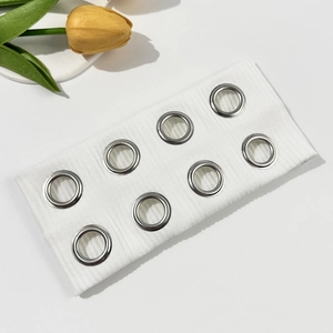 Close-up of white ribbed knit headband with silver metal eyelets and hollow rings detail